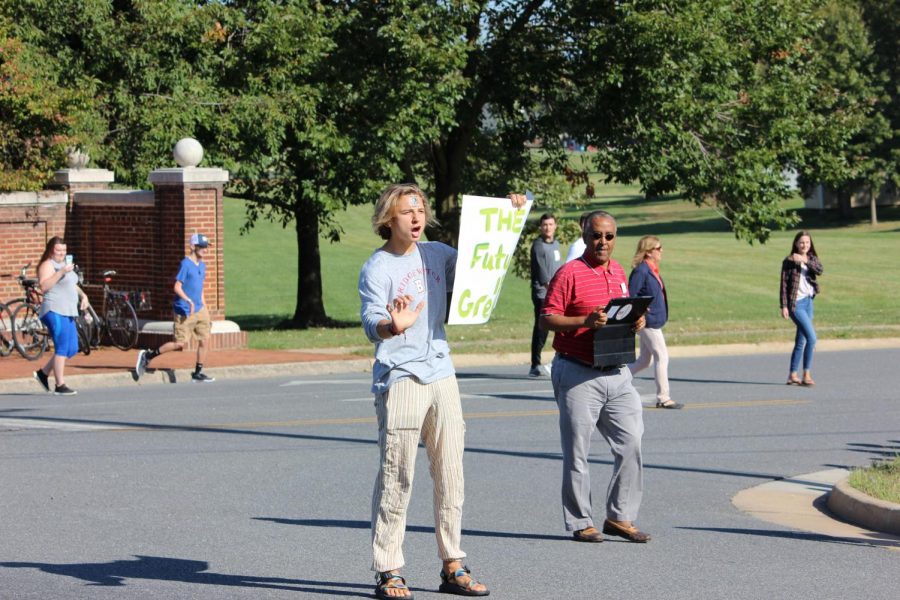 Hunter Potts (center) stands in the street, asking drivers to honk for climate change, while Teshome Molalenge (right) looks on with his tablet.