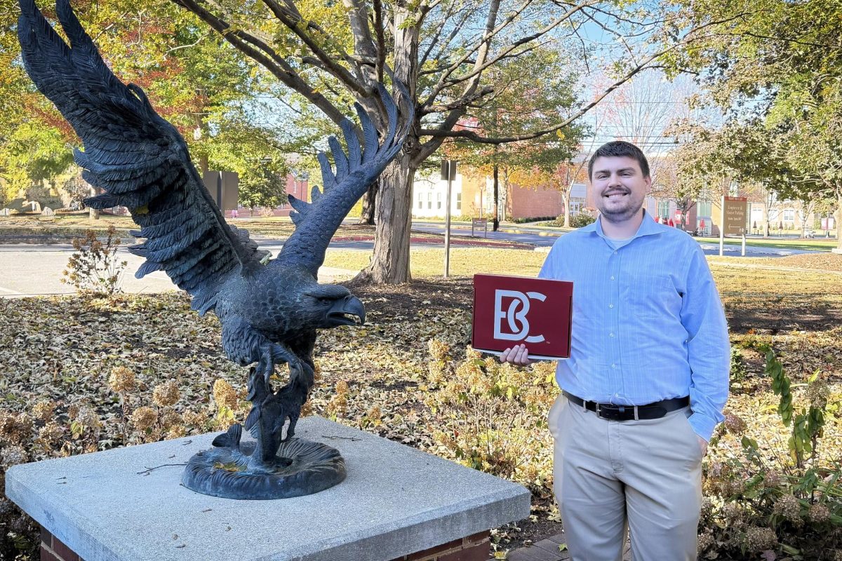 Jason Newell stands in front of the Yount Hall eagle statue with a Bridgewater College admissions box. These boxes are sent out to all admitted students, many of whom tour the college and pose with the same statue.