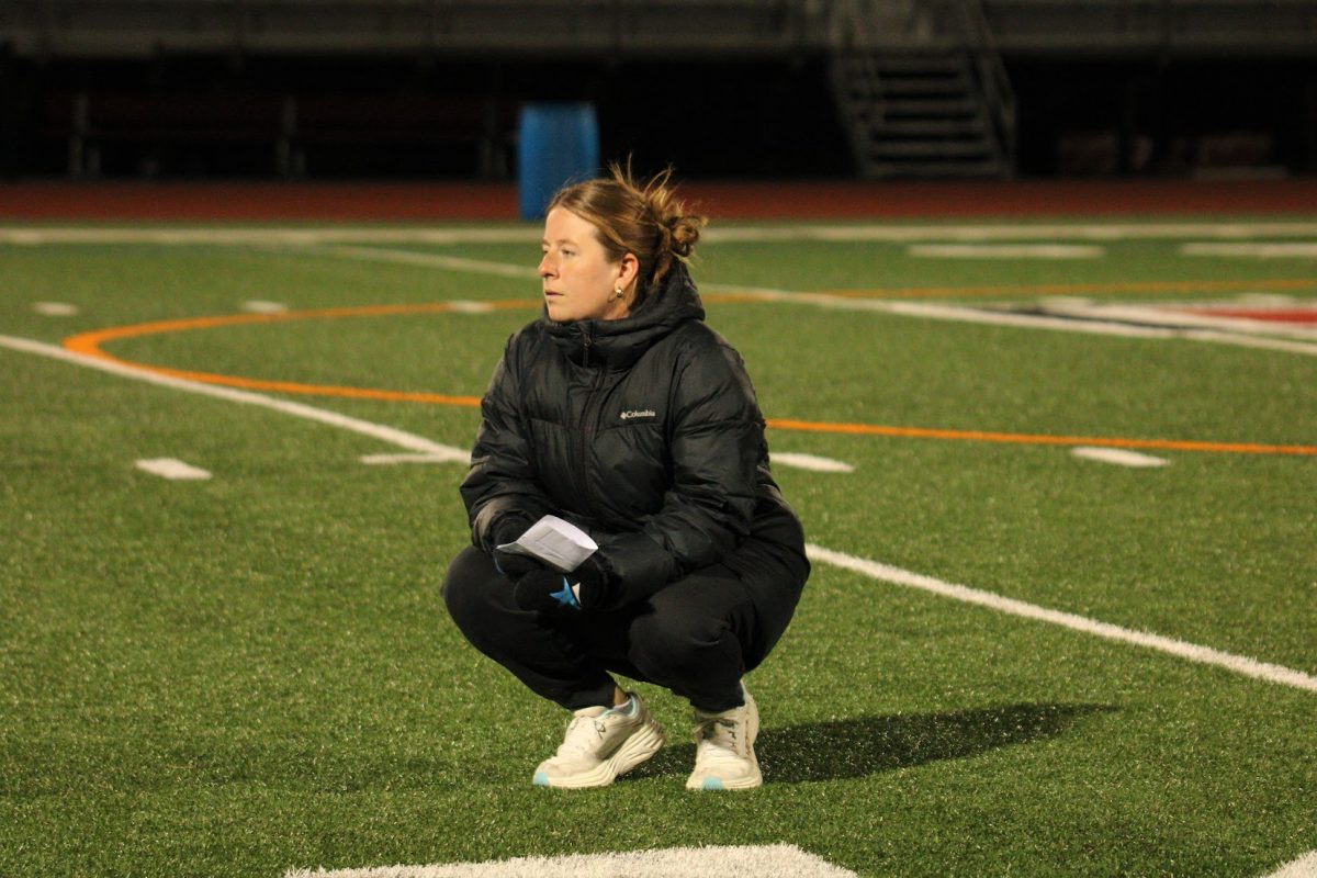 Coach Emily Bagby crouches while she cheers on players during a drill. Bagby emphasizes being a cheerleader for her team during everything, even practices.